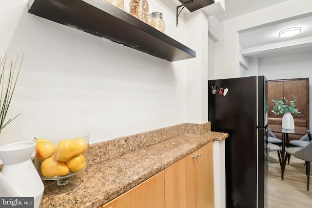 kitchen featuring black fridge, light stone countertops, and light wood-type flooring