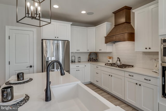 kitchen with premium range hood, white cabinetry, appliances with stainless steel finishes, and decorative light fixtures