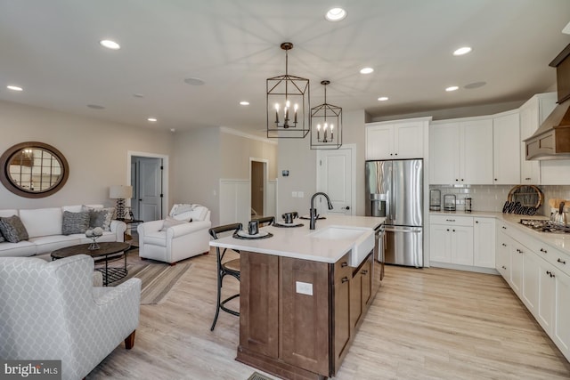 kitchen featuring stainless steel appliances, white cabinetry, a center island with sink, and decorative light fixtures