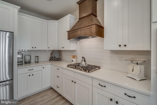 kitchen featuring appliances with stainless steel finishes, white cabinetry, backsplash, custom range hood, and light hardwood / wood-style flooring