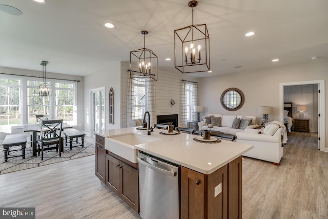 kitchen with decorative light fixtures, dishwasher, sink, a kitchen island with sink, and light hardwood / wood-style flooring