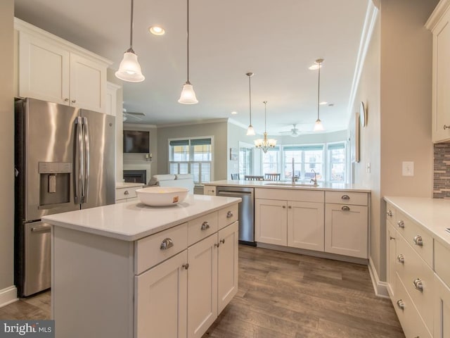 kitchen with a center island, hanging light fixtures, appliances with stainless steel finishes, kitchen peninsula, and white cabinets