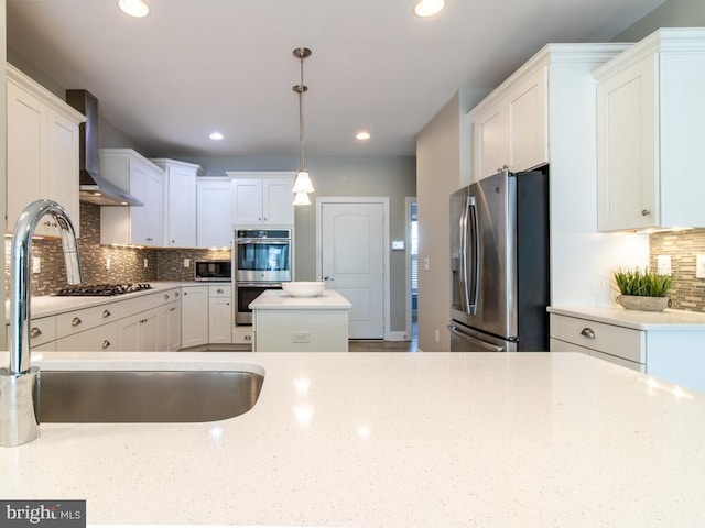 kitchen with wall chimney exhaust hood, sink, appliances with stainless steel finishes, pendant lighting, and white cabinets