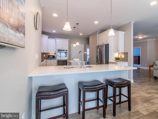 kitchen featuring sink, hanging light fixtures, stainless steel appliances, white cabinets, and a kitchen bar