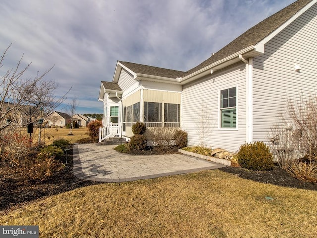 view of side of home featuring a sunroom, a yard, and a patio area