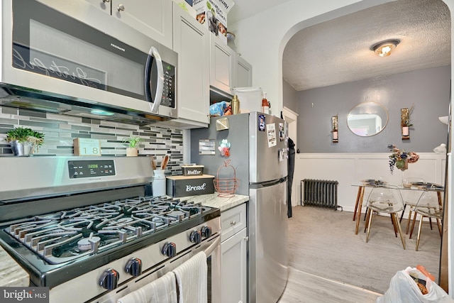 kitchen featuring white cabinetry, a textured ceiling, radiator heating unit, stainless steel appliances, and decorative backsplash