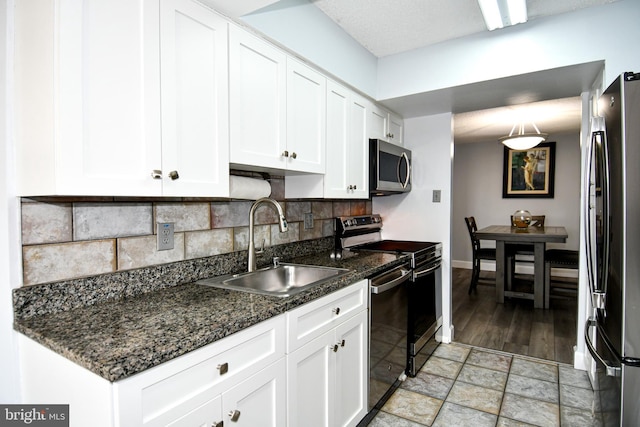 kitchen with white cabinetry, sink, dark stone counters, decorative backsplash, and stainless steel appliances