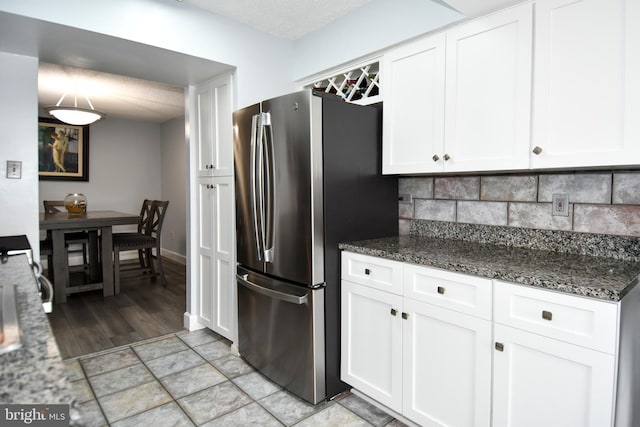 kitchen featuring stainless steel fridge, dark stone countertops, and white cabinets