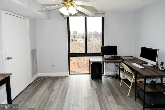 office space featuring expansive windows, ceiling fan, light hardwood / wood-style floors, and a textured ceiling