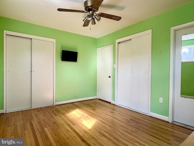 unfurnished bedroom featuring two closets, a ceiling fan, baseboards, and wood finished floors