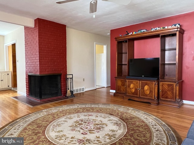 living area with baseboards, visible vents, ceiling fan, wood finished floors, and a brick fireplace