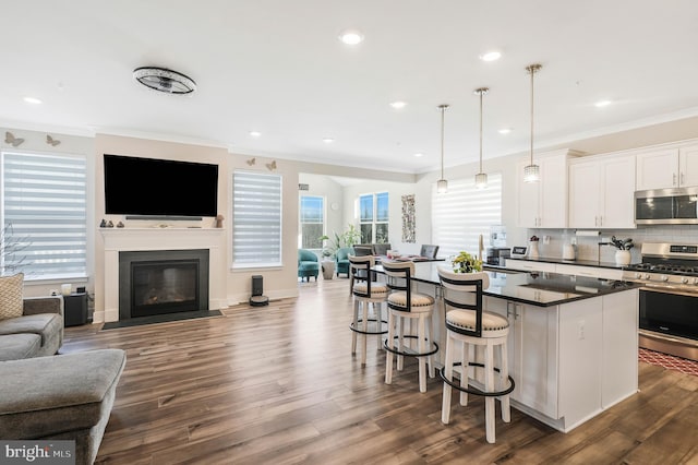 kitchen featuring a kitchen island, appliances with stainless steel finishes, decorative light fixtures, white cabinets, and a kitchen breakfast bar