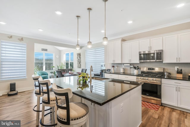 kitchen featuring appliances with stainless steel finishes, white cabinets, decorative backsplash, hanging light fixtures, and a center island with sink