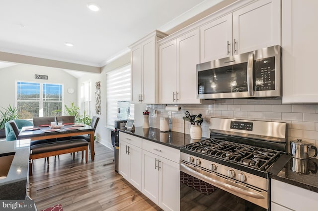 kitchen with white cabinetry, backsplash, stainless steel appliances, and dark stone counters