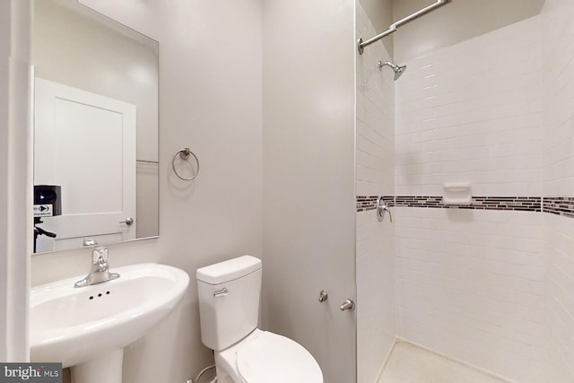 bathroom featuring a tile shower, sink, and toilet