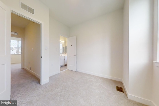 unfurnished bedroom featuring light colored carpet and ensuite bath