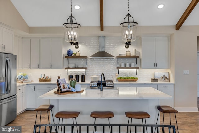 kitchen with wall chimney exhaust hood, a center island with sink, appliances with stainless steel finishes, a kitchen breakfast bar, and white cabinets