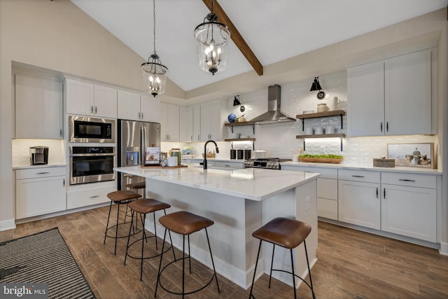 kitchen featuring a breakfast bar area, a kitchen island with sink, stainless steel appliances, white cabinets, and wall chimney exhaust hood