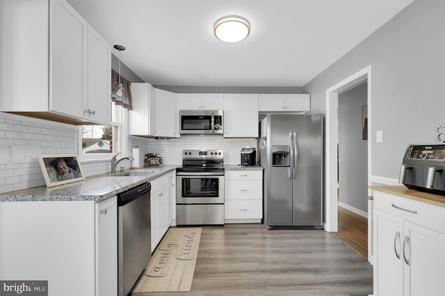 kitchen featuring sink, light hardwood / wood-style flooring, appliances with stainless steel finishes, white cabinetry, and light stone countertops