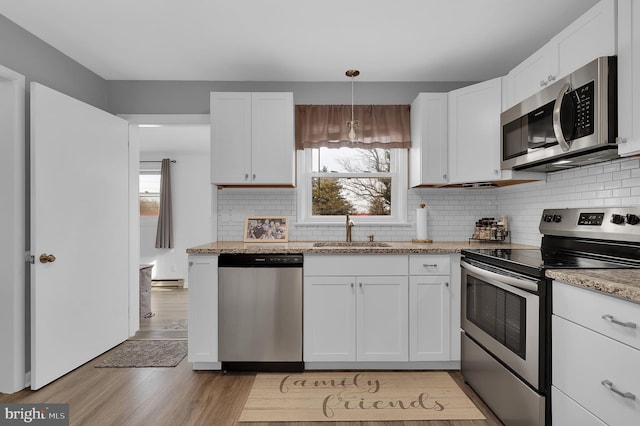 kitchen featuring appliances with stainless steel finishes, white cabinetry, sink, hanging light fixtures, and light stone counters