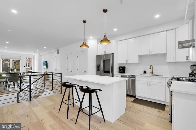 kitchen with stainless steel appliances, light countertops, white cabinets, a sink, and a kitchen island