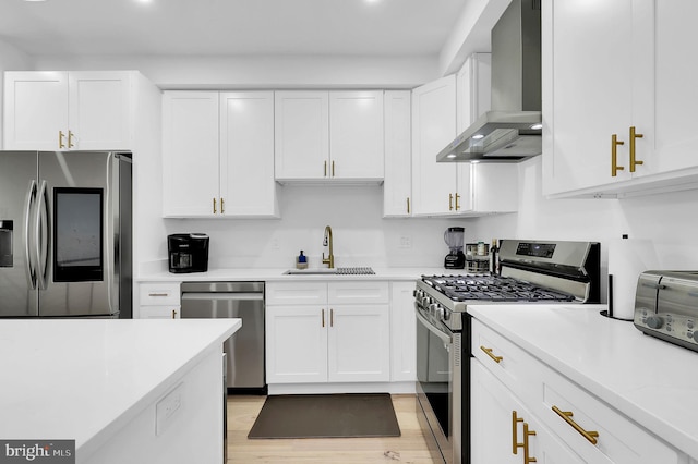 kitchen featuring appliances with stainless steel finishes, light countertops, wall chimney range hood, white cabinetry, and a sink