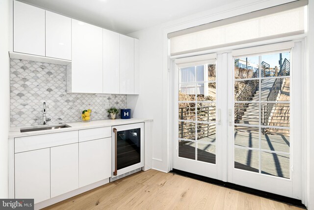 kitchen featuring wine cooler, sink, light hardwood / wood-style flooring, white cabinets, and backsplash