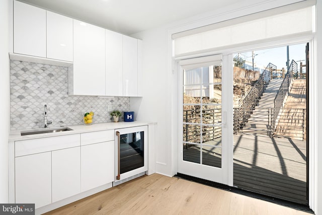 kitchen with sink, white cabinetry, beverage cooler, light hardwood / wood-style floors, and backsplash