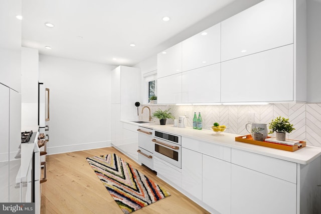 kitchen featuring sink, white cabinets, backsplash, white oven, and light hardwood / wood-style flooring