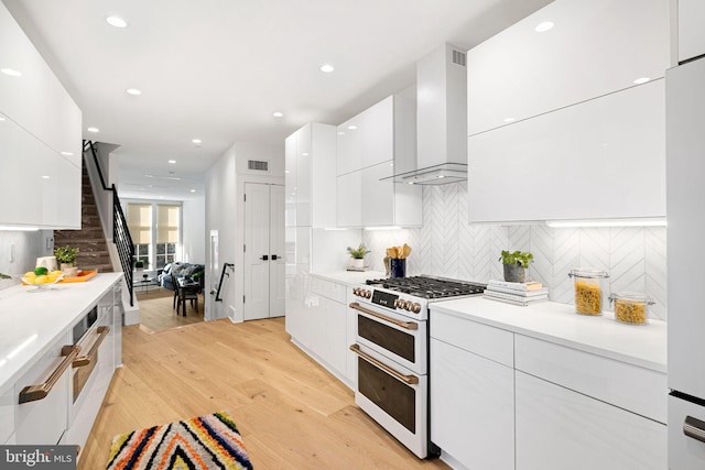 kitchen with wall chimney range hood, white appliances, white cabinetry, decorative backsplash, and light wood-type flooring