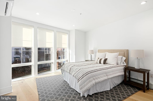 bedroom with hardwood / wood-style flooring, a baseboard radiator, and a wall unit AC