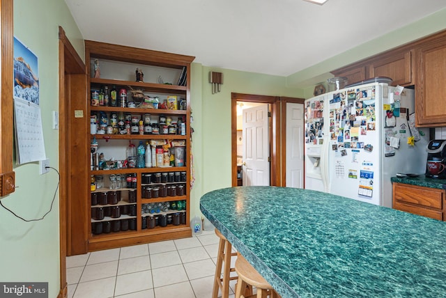 kitchen featuring light tile patterned flooring, white fridge with ice dispenser, and a kitchen breakfast bar