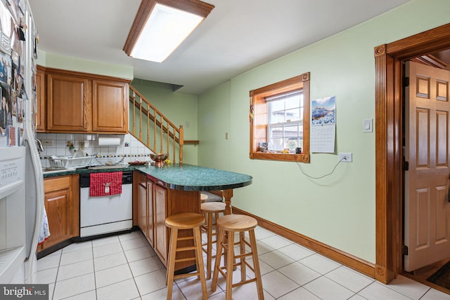 kitchen with backsplash, a kitchen bar, light tile patterned floors, white dishwasher, and kitchen peninsula