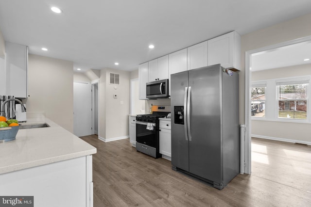 kitchen with sink, hardwood / wood-style floors, white cabinetry, and stainless steel appliances