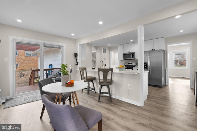 kitchen with a breakfast bar, light hardwood / wood-style floors, stainless steel appliances, kitchen peninsula, and white cabinets