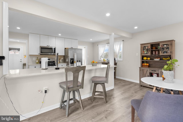 kitchen with light hardwood / wood-style flooring, a breakfast bar, stainless steel appliances, kitchen peninsula, and white cabinets