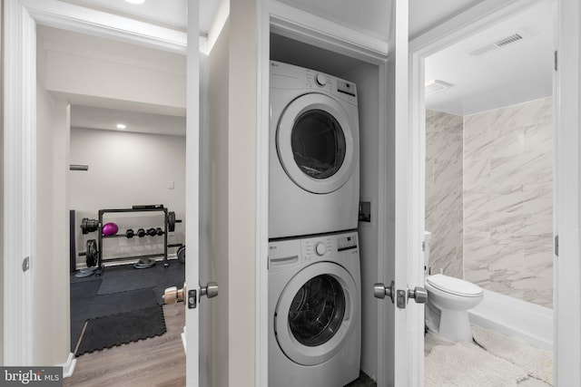 clothes washing area with light hardwood / wood-style flooring and stacked washer / drying machine