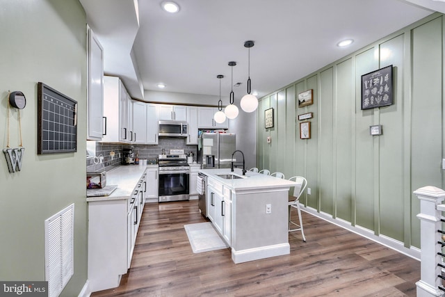 kitchen featuring appliances with stainless steel finishes, hanging light fixtures, tasteful backsplash, an island with sink, and white cabinets