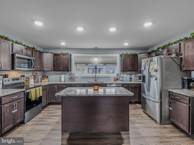 kitchen featuring sink, dark brown cabinets, stainless steel appliances, a kitchen island, and decorative light fixtures