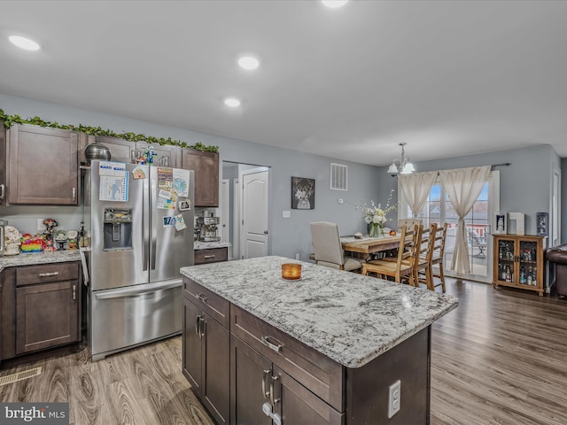 kitchen featuring a kitchen island, decorative light fixtures, stainless steel fridge, dark brown cabinetry, and light wood-type flooring