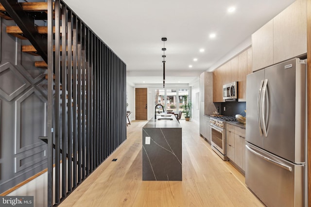 kitchen with appliances with stainless steel finishes, light brown cabinetry, decorative light fixtures, sink, and light hardwood / wood-style flooring