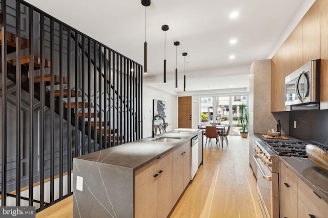 kitchen with appliances with stainless steel finishes, sink, hanging light fixtures, and light hardwood / wood-style flooring