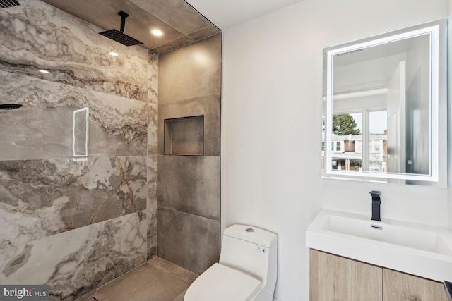 bathroom featuring vanity, a tile shower, and toilet