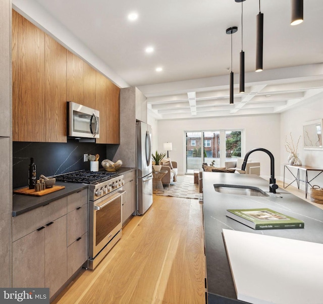 kitchen featuring sink, hanging light fixtures, light wood-type flooring, appliances with stainless steel finishes, and decorative backsplash