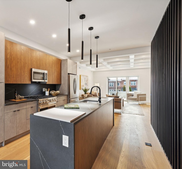 kitchen featuring appliances with stainless steel finishes, sink, hanging light fixtures, a kitchen island with sink, and light hardwood / wood-style floors