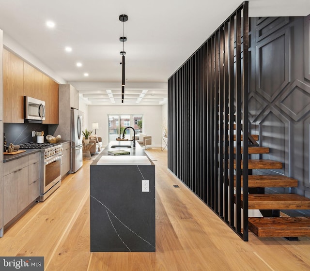 kitchen with appliances with stainless steel finishes, pendant lighting, sink, backsplash, and light hardwood / wood-style flooring