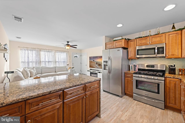 kitchen with ceiling fan, stainless steel appliances, light stone countertops, light hardwood / wood-style floors, and decorative backsplash