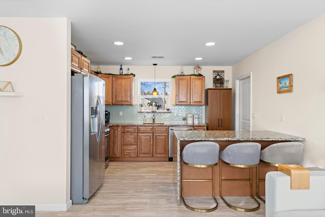 kitchen featuring a breakfast bar area, light stone counters, pendant lighting, stainless steel appliances, and decorative backsplash