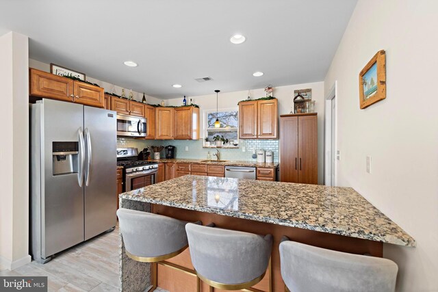 kitchen featuring appliances with stainless steel finishes, tasteful backsplash, sink, hanging light fixtures, and light stone counters