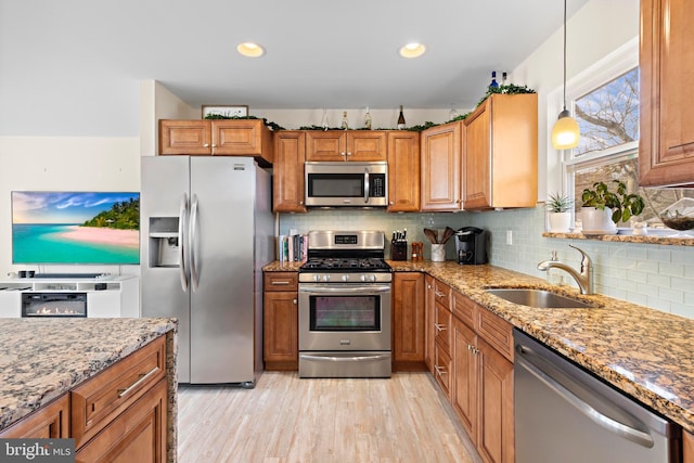 kitchen with pendant lighting, sink, light stone countertops, and appliances with stainless steel finishes